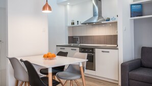 Une cuisine moderne avec des armoires blanches, une hotte en acier inoxydable et un coin repas comprenant une table et des chaises blanches.
