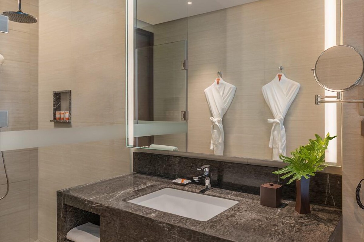 A modern bathroom with a marble sink, a large mirror, and two white robes hanging on hooks.