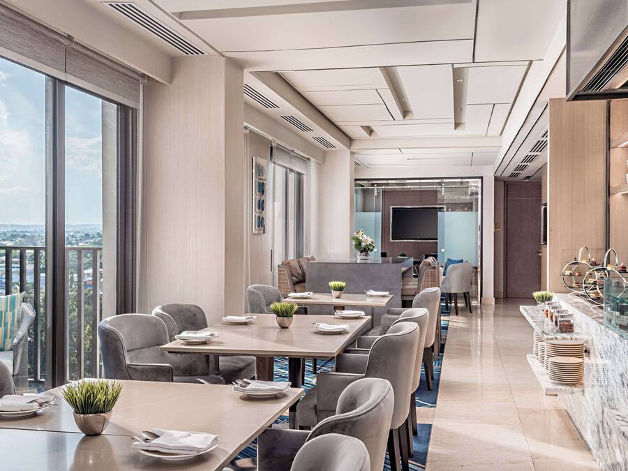 Un comedor de hotel moderno con ventanas amplias, un balcón y una cocina al fondo.