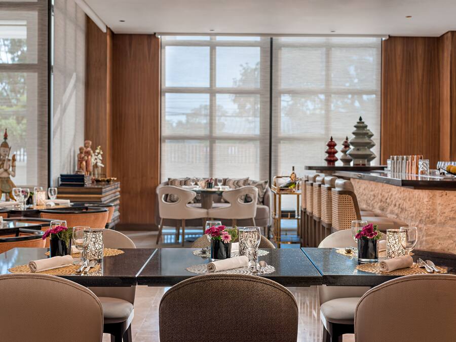 A modern dining area with a glass table, wicker chairs, and a view of the outdoors through large windows.