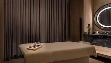 Relax in a serene spa room with a massage table, sink, and mirror.