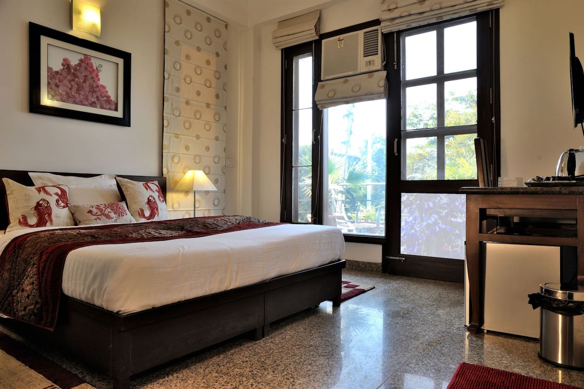 A bedroom with a bed, a desk, a trash bin, a window with a view, and a wall-mounted air conditioner.