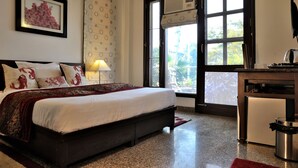 A bedroom with a bed, a desk, and a trash bin. - Redbrick villa (Gurugram)