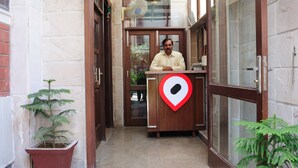 A reception area with a receptionist, a potted plant, and a location pin on the counter. - Redbrick villa (Gurugram)