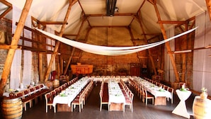 A large hall with long tables set for dining, wooden beams, and rustic brick walls. - Hotel Wenzels Hof (Beilrode)