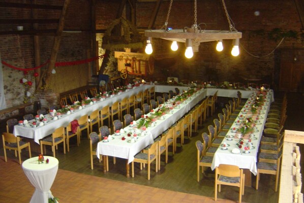 A long banquet hall with multiple tables set for a formal event, wooden chairs, and hanging light fixtures. - Hotel Wenzels Hof (Beilrode)