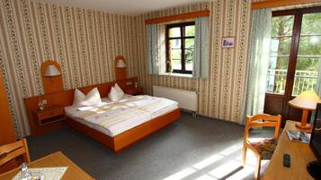 A hotel room with a bed, a desk, a chair, a window with curtains, and a radiator.