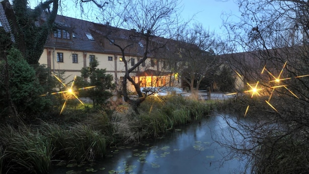 A riverside building with a traditional architectural style, surrounded by natural vegetation and a calm water body. - Hotel Wenzels Hof (Beilrode)