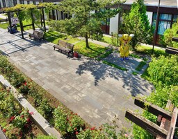 Un parque con un sendero pavimentado, bancos, una escultura y macizos de flores.