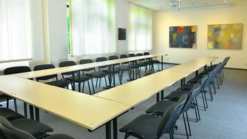 A conference room with a long table and chairs, large windows with blinds, and abstract paintings on the walls.