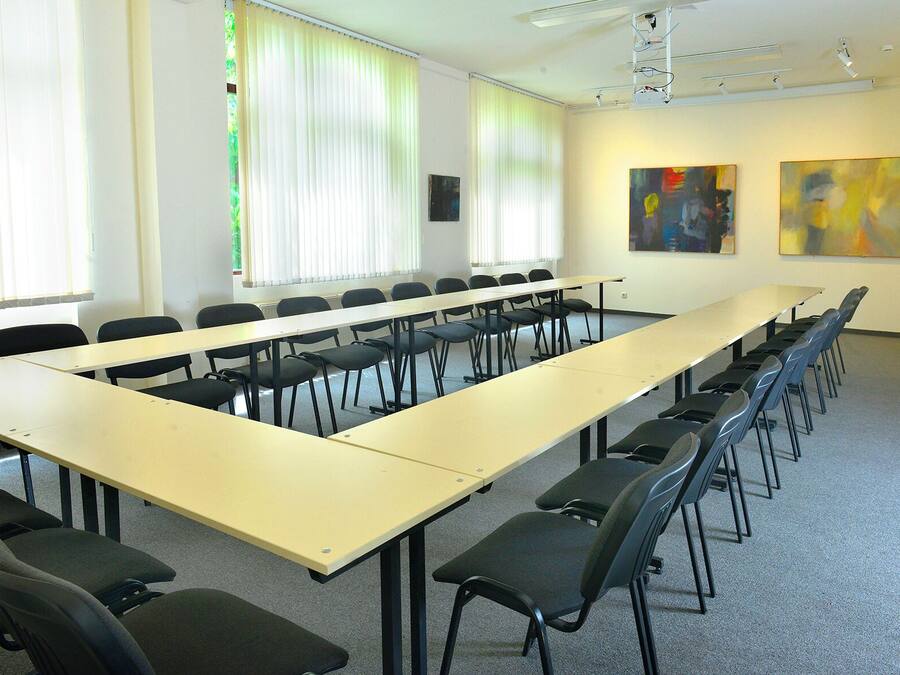 A conference room with a long table and chairs, large windows with blinds, and abstract paintings on the walls.