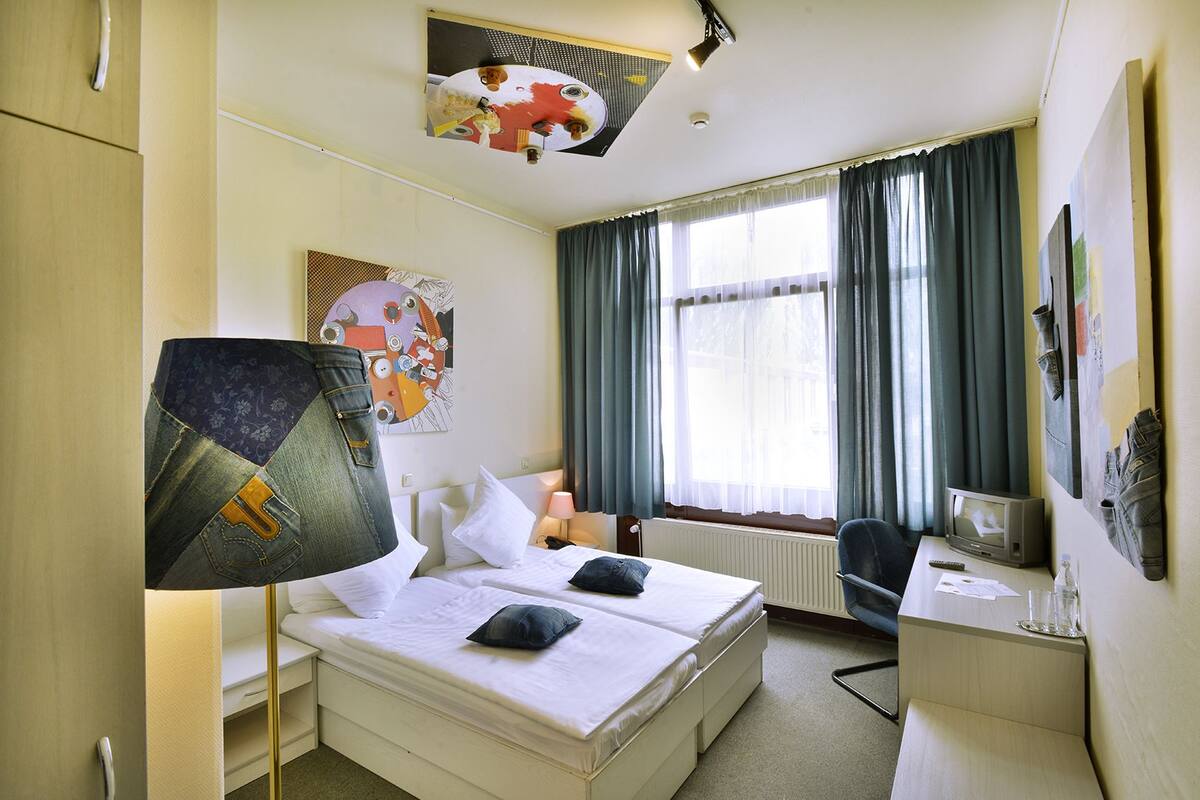 Une chambre d’hôtel avec un lit, un bureau, une chaise, une lampe et un téléviseur.