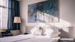 A hotel room with a bed, a bedside table, a lamp, a chair, and a painting on the wall. - Berlin Art Hotel (Gyumri)