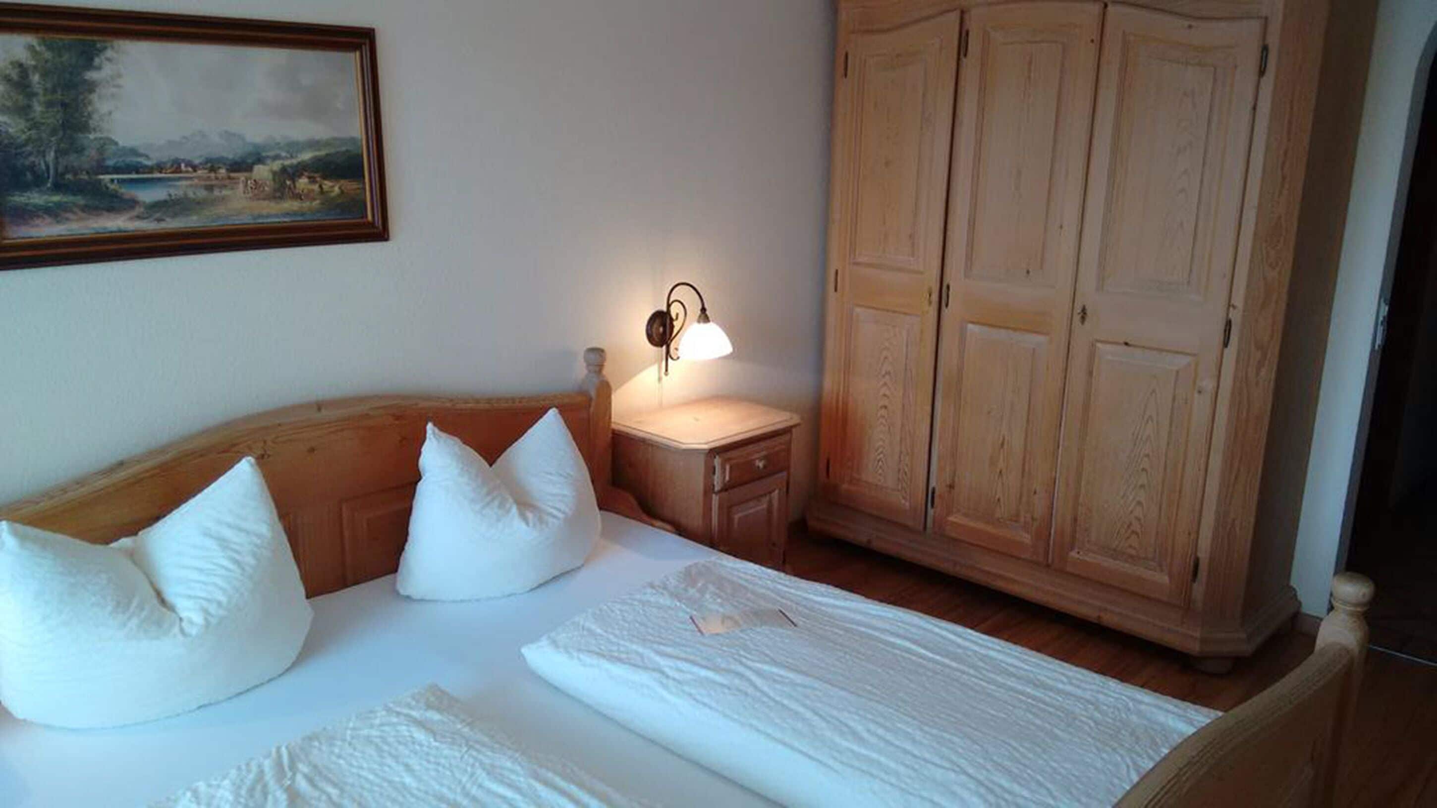 Un dormitorio con una cama de madera, ropa de cama blanca, una mesita de noche con una lámpara y un armario.