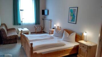 Ein Hotelzimmer mit Doppelbett, Schreibtisch, Stuhl, kleinen Tisch, Lampe und einem Bild an der Wand.