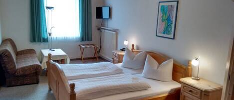 Ein Hotelzimmer mit Doppelbett, Schreibtisch, Stuhl, kleinen Tisch, Lampe und einem Bild an der Wand.