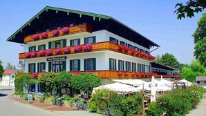 Un edificio de dos plantas con balcones decorados con flores, un letrero que indica que es un restaurante y mesas al aire libre con sombrillas.