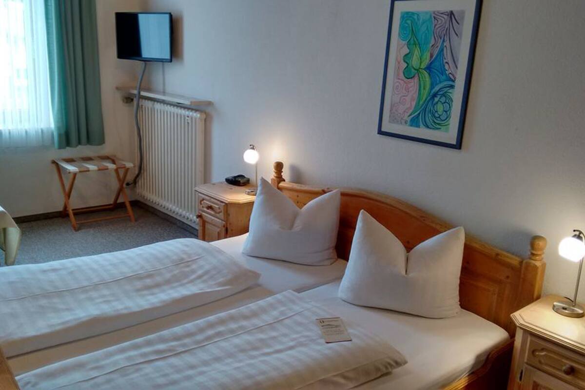 Une chambre d’hôtel avec deux lits, un bureau, une chaise, un radiateur, une télévision et un tableau au mur.