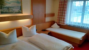 A hotel room with two single beds, a wooden headboard, a nightstand, a painting on the wall, and a window with a plaid curtain.