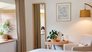 Hotellihuone, jossa on sänky, yöpöytä, lamppu, ruukkukasvi ja seinällä oleva kehystetty taideteos.