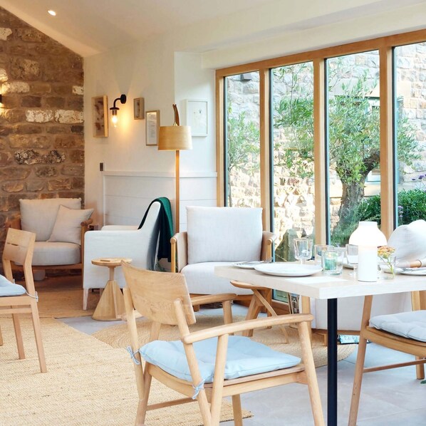 A modern dining area with wooden furniture, a stone wall, and large windows offering a view of greenery. - Lancaster Barn B&B (Lancaster)