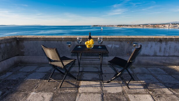 A terrace with a table and two chairs, overlooking a coastal cityscape. - Apartment Veduta (Zadar)