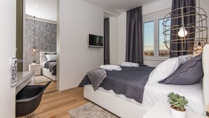 A modern bedroom with a bed, bedside table, TV, and a view of the city. - Apartment Veduta (Zadar)