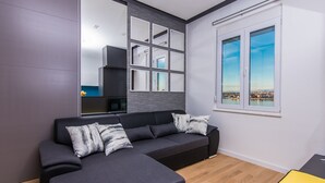 A modern living room with a sectional sofa, a large mirror, and a window with a city view. - Apartment Veduta (Zadar)