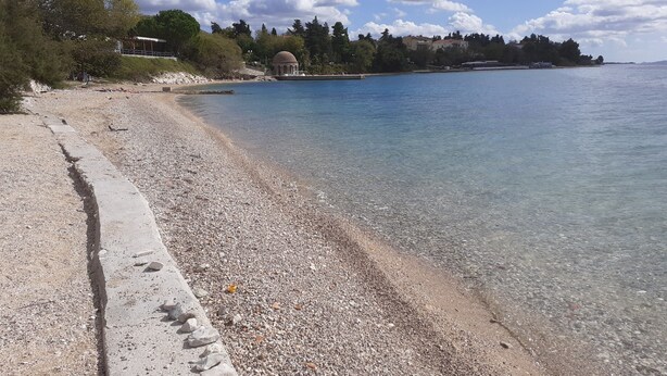 A pebbled beach with a clear view of the sea and a dome structure in the background. - Sunset Beach Apartment (Zadar)
