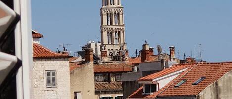 A historic building with a prominent bell tower, surrounded by traditional red-tiled roofs and stone buildings.