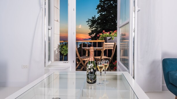 Een balkon met een glazen tafel, een fles champagne en twee glaasjes.