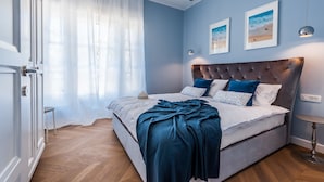 Een slaapkamer met een groot bed, een nachtkastje, een stoel en een raam met dunne gordijnen.