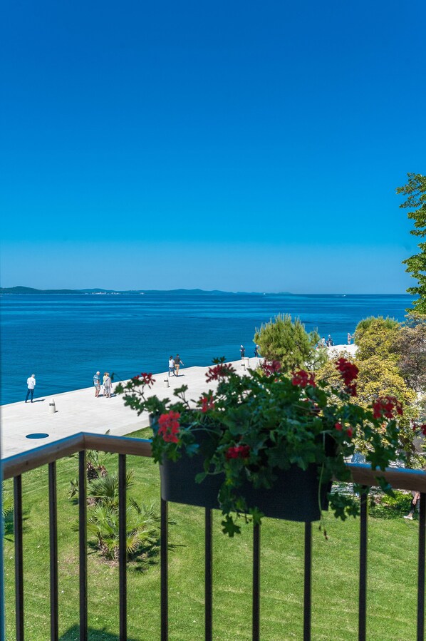 Relax in a serene outdoor space with a clear view of the sea, surrounded by a well-maintained lawn and lush greenery.
