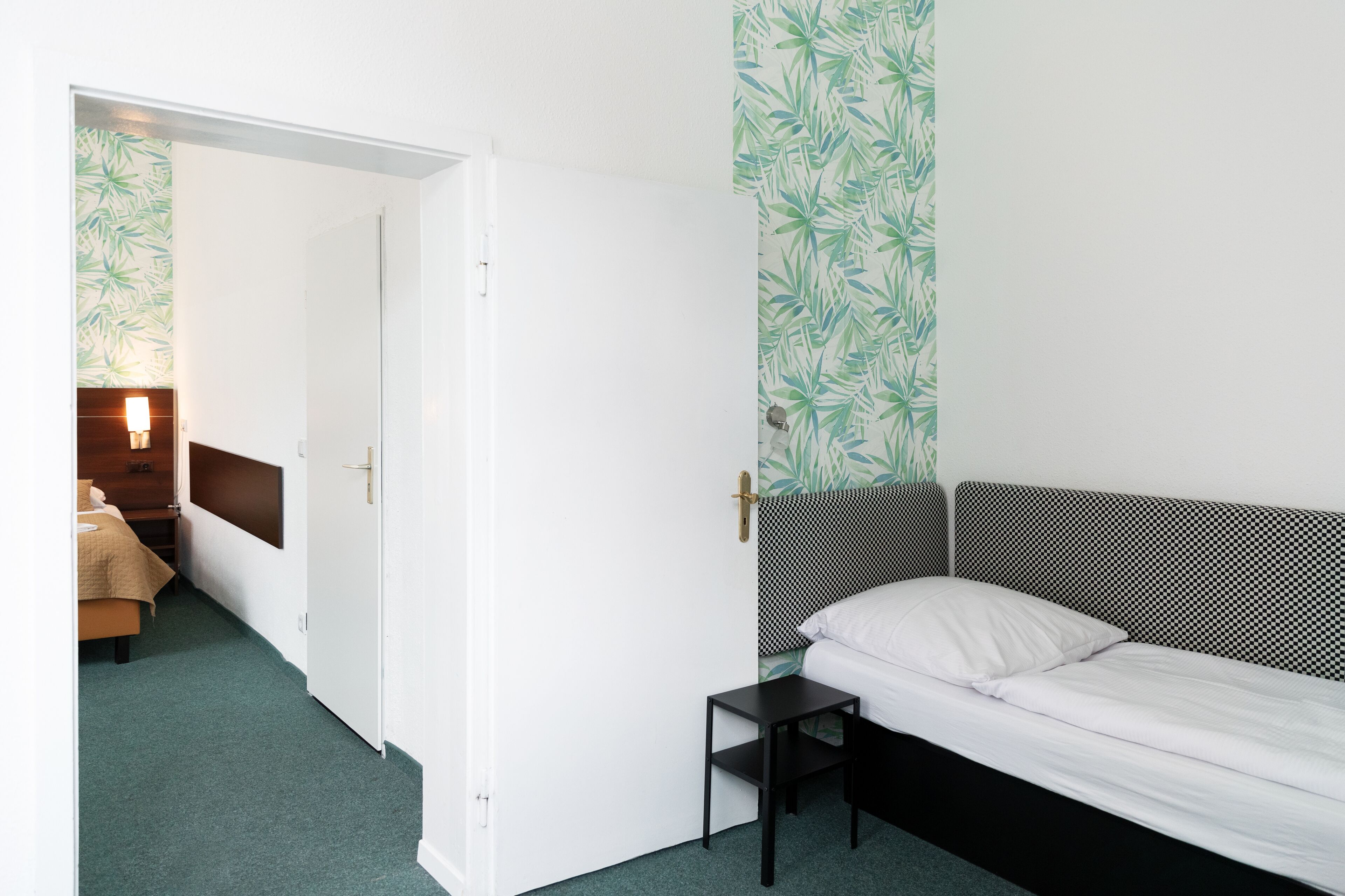 Un dormitorio con una cama, una mesita de noche y una puerta que da a otra habitación.