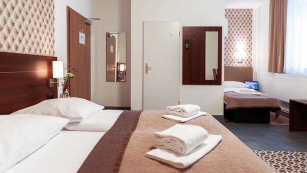 Habitación de hotel con una cama grande, otra más pequeña, un escritorio, una silla, una lámpara, un espejo y una ventana con cortinas.