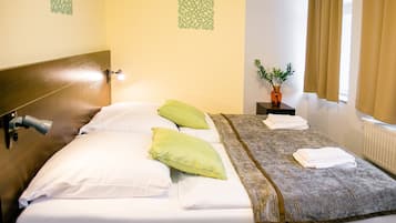 Una cama bien hecha con almohadas blancas y verdes, una manta gris y una mesita con un florero.