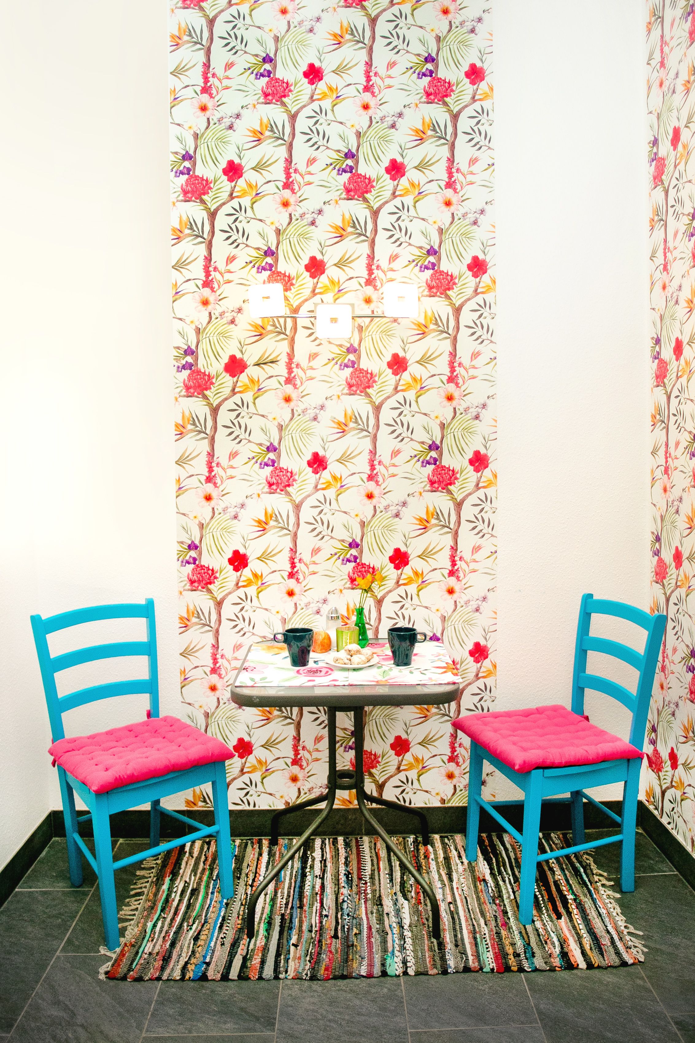 Ein Eckzimmer mit zwei blauen Stühlen, einem kleinen Tisch mit Blumenmuster und einem Teppich mit Muster.