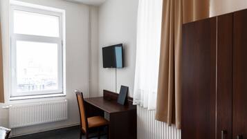 A room with a desk, chair, and a television mounted on the wall.