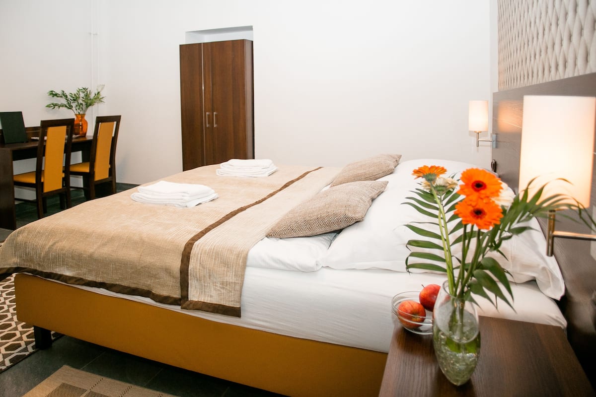 Habitación de hotel con cama, escritorio y silla. En la mesita de noche hay un florero con flores.