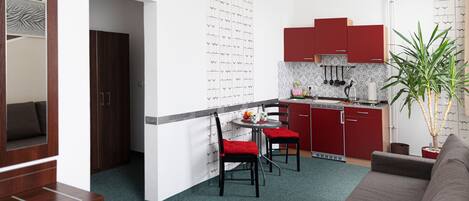 Un espacio habitable compacto con kitchenette, una zona de comedor con dos sillas, un sofá y una planta en maceta.