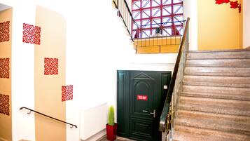 A staircase with a handrail, a red door with a sign, and a window with a red grid pattern.