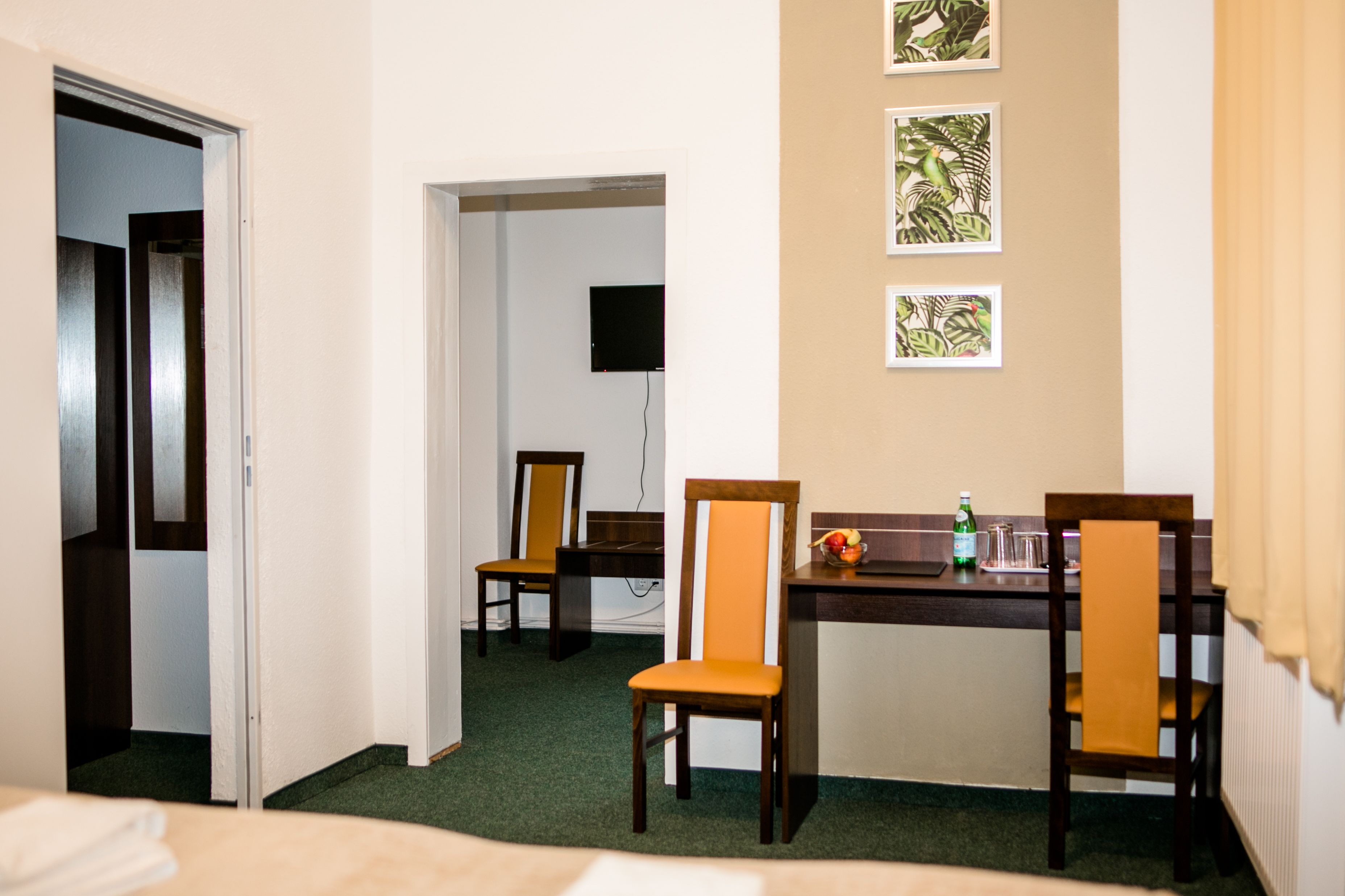 A hotel room with a bed, a desk with two chairs, a television, and framed pictures on the wall.