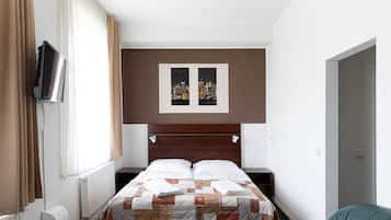 Habitación de hotel con cama, televisor montado en la pared, ventana con cortinas y una imagen de un paisaje urbano sobre la cama.