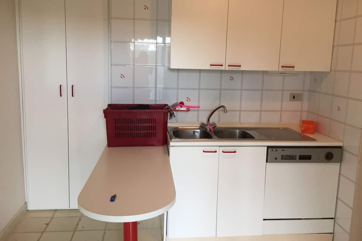 A compact kitchen with white cabinets, a red plastic basket, a sink, and a dishwasher.