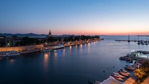 A waterfront cityscape at dusk with a calm river, boats, and a distant tower. - Amazing View Apartment (Zadar)