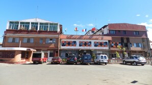 Un hotel con un cartello che recita 'HOTEL DIAMANT' e un cartello con scritto 'KARAOKE' sotto. Diversi veicoli sono parcheggiati davanti.