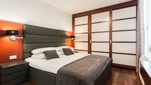 Une chambre à coucher moderne avec un grand lit, une table de chevet, une lampe fixée au mur et une armoire à portes coulissantes.