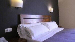 Una habitación de hotel con cabecera de madera, ropa de cama blanca y dos lámparas fijadas a la pared.