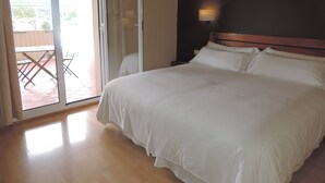 Un dormitorio con cama, mesita de noche, lámpara y puerta corrediza de vidrio que da a un patio exterior.