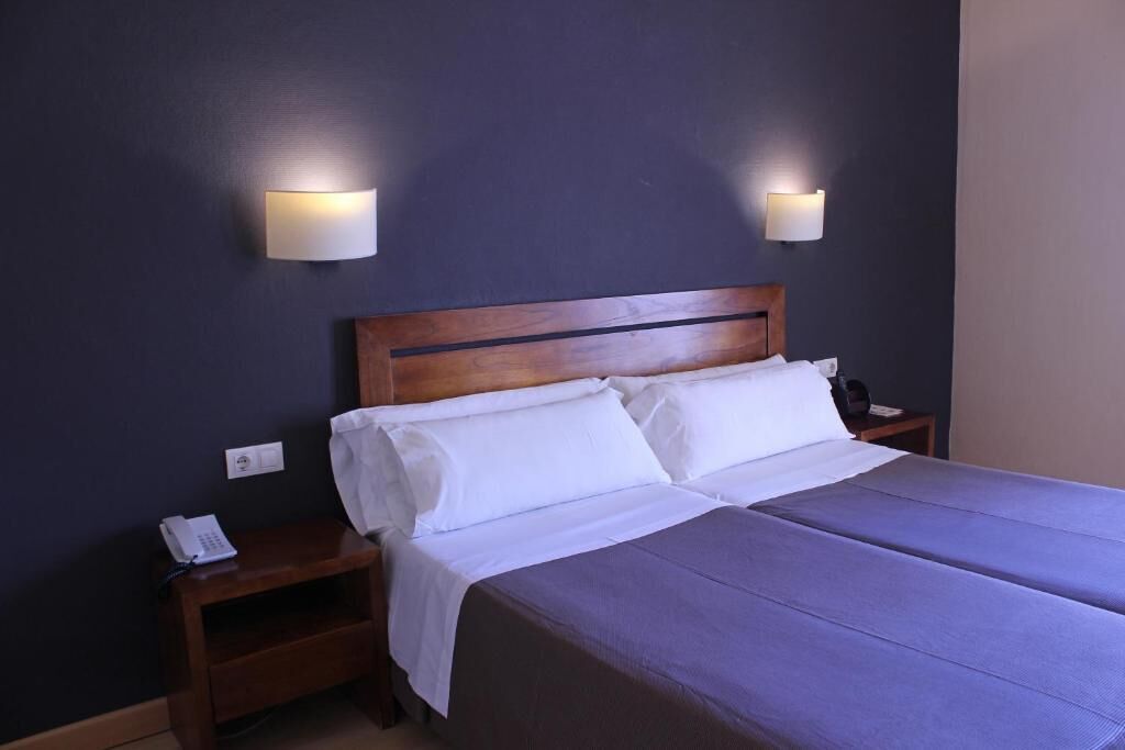 A hotel room with a double bed, two bedside tables, a nightstand, and two wall-mounted lamps.